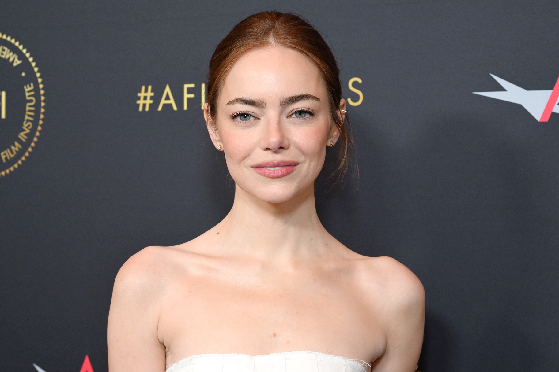 Emma Stone smiling in a white dress at the AFI Awards.