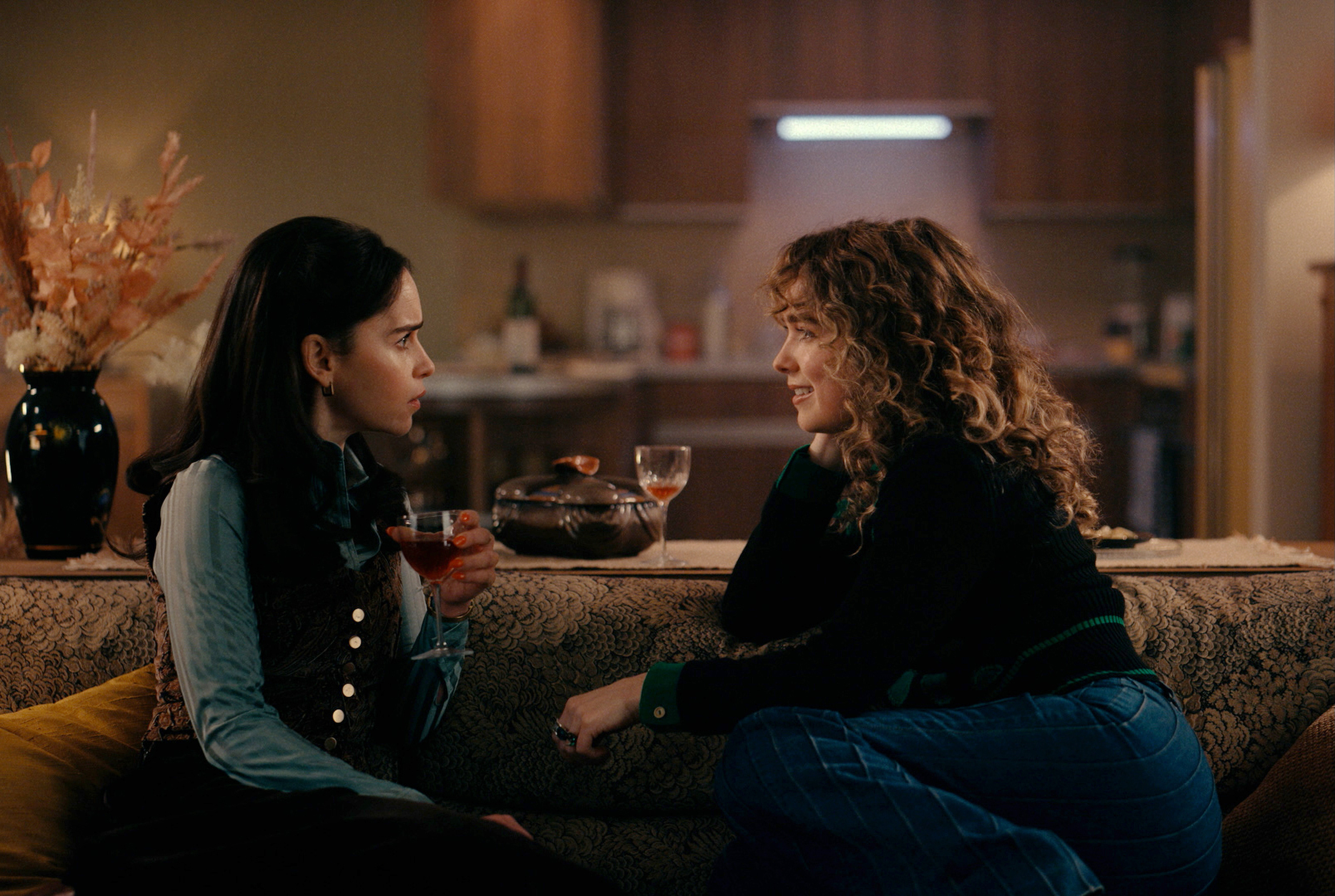 Bea (Emilia Clarke) and Twila (Haley Lu Richardson) sitting on a couch together during Ponies Season 1.