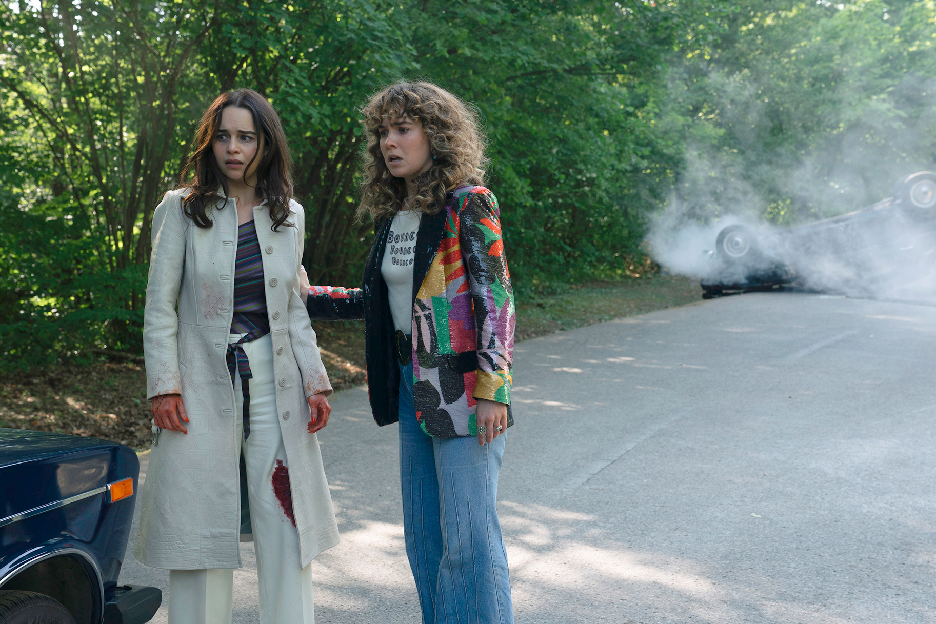 Bea and Twila standing outside by a car and smoke behind them in PONIES Season 1 Episode 8.