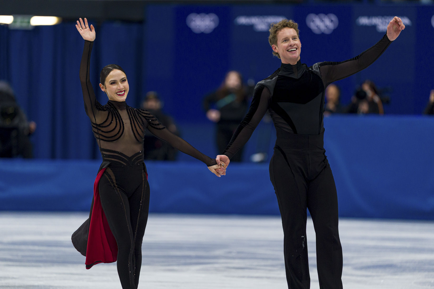 Madison Chock and Evan Bates wave while on the ice at the 2026 Milan Cortina Olympics.