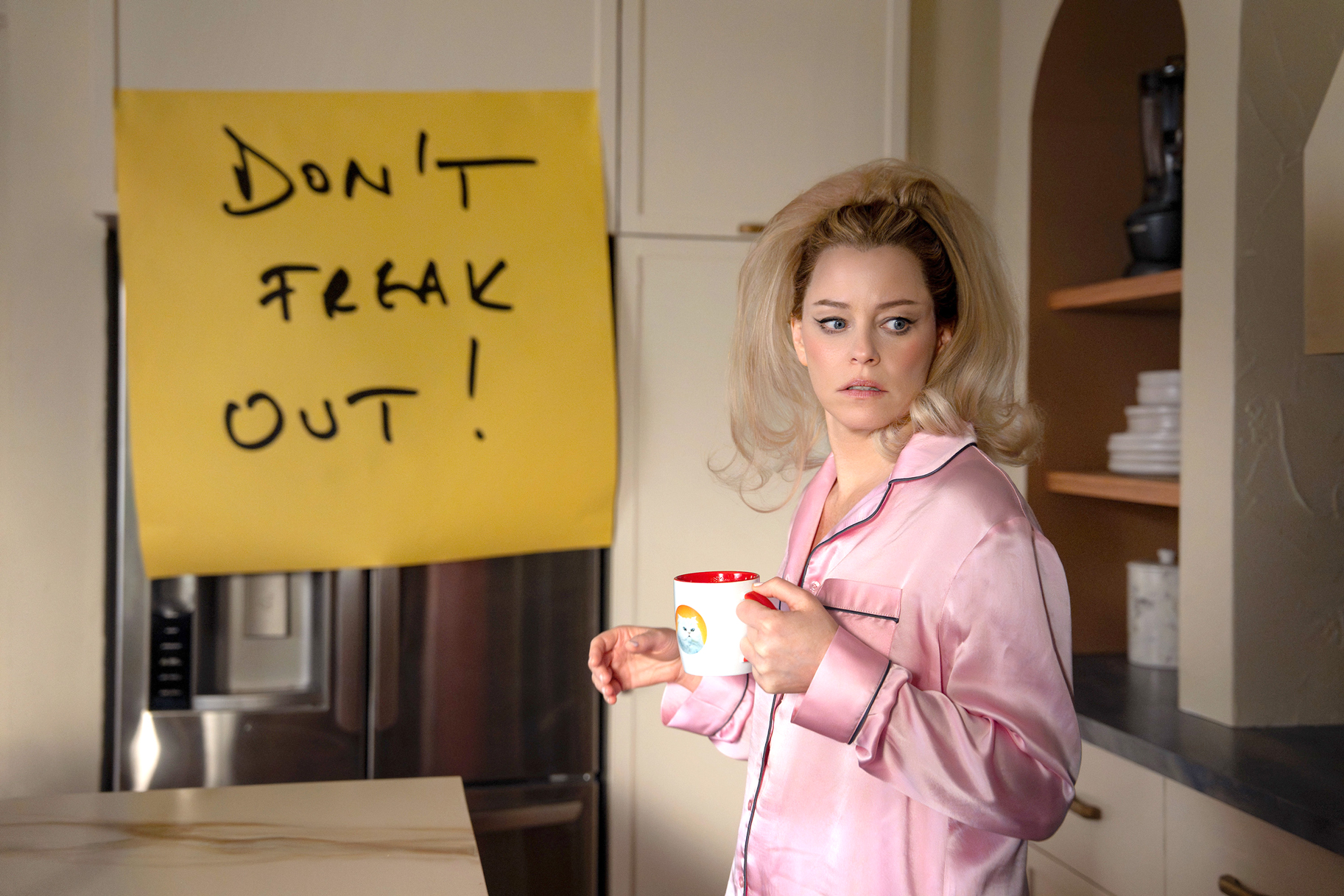 Elizabeth Banks wearing a pink pajama top and holding a mug of coffee on The Miniature Wife.