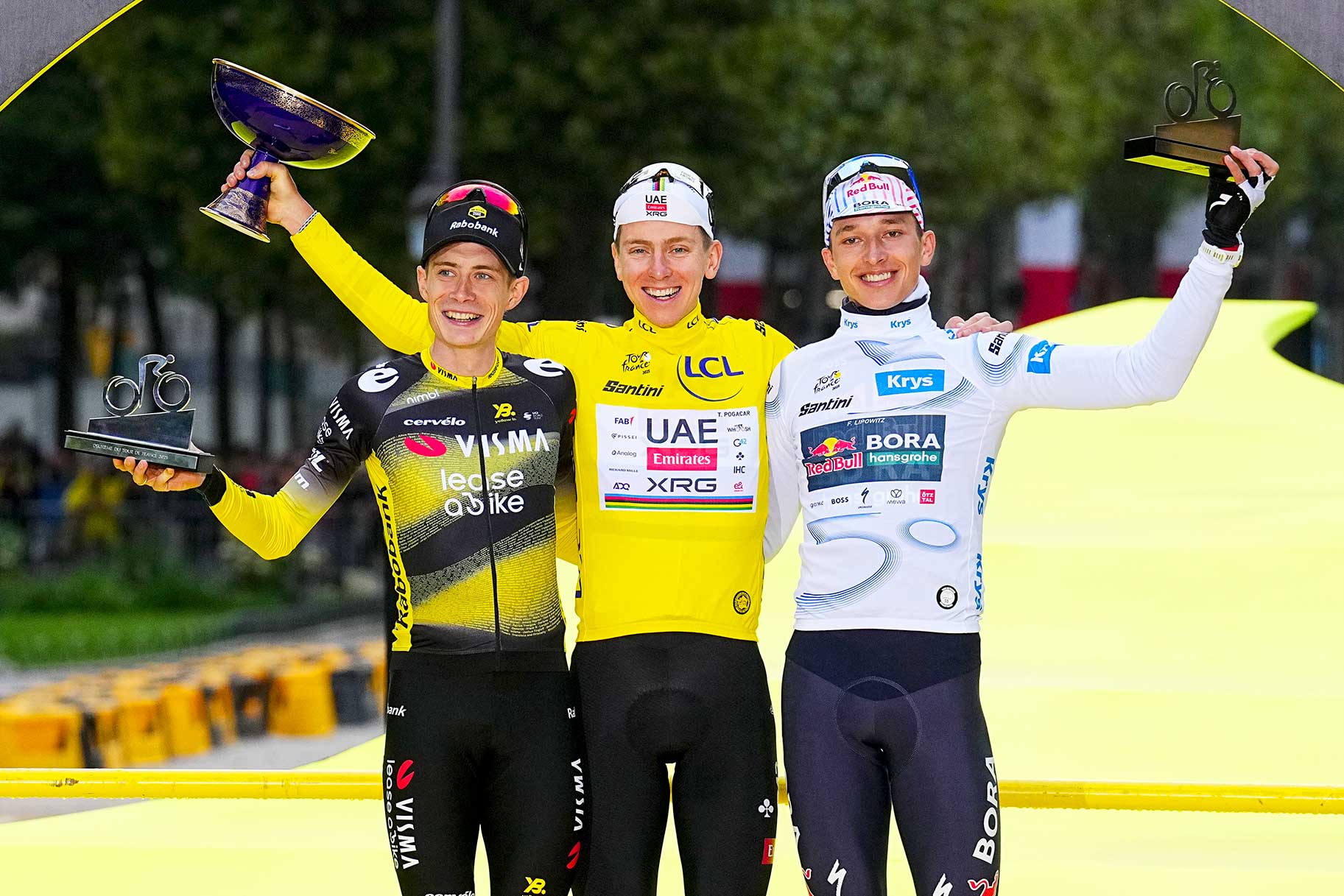 Jonas Vingegaard, Tadej Pogacar, and Florian Lipowitz celebrating and holding trophies at the Tour de France 2025.