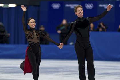 Madison Chock and Evan Bates wave while on the ice at the 2026 Milan Cortina Olympics.