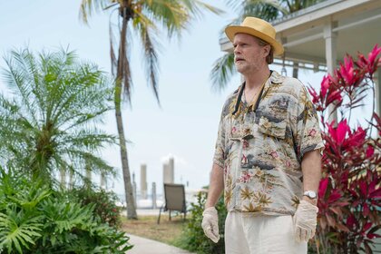 Kincaid looking while outside surrounded by flowers and palm trees in M.I.A. Season 1 Episode 2.