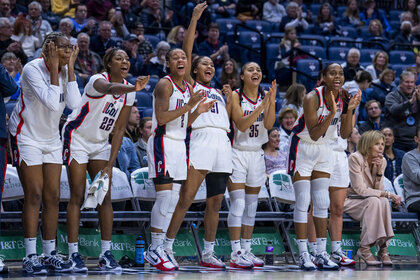 The Connecticut Huskies players cheer on the sidelines of a basketball game.