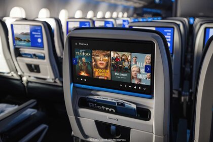 Rows of the back of seats on a United Airlines flight with screens displaying Peacock movies and tv series