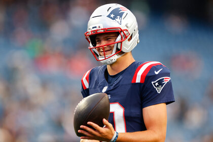 Drake Maye wearing his New England Patriots unifrom and holding a football in his hand.