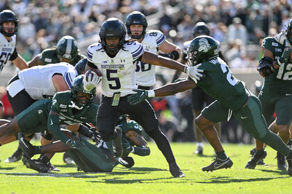 Northwestern Wildcats running back Joseph Himon II carries the ball and stiff-arms Michigan State Spartans safety Devin Vaught during a football game.