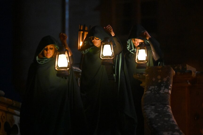 Candiace Dillard Bassett, Lisa Rinna, and Rob Rausch stand in hoods while holding lanterns on The Traitors Episode 401.