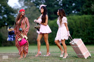 Three women outside in pink dresses wheeling a pink suitcase on The Real Housewives of Rhode Island