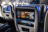 Rows of the back of seats on a United Airlines flight with screens displaying Peacock movies and tv series