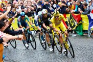 A group of bikers going up a stone street with a crowd a people cheering during the 112th Tour de France.