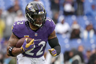 Derrick Henry of the Baltimore Ravens holding a football and running the field during a football game.