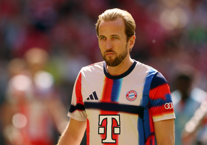 Harry Kane standing in a soccer stadium in front of fans in the background.