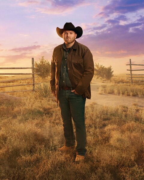 Cole McBee standing in front of a farm field, trees, and dusk skies.