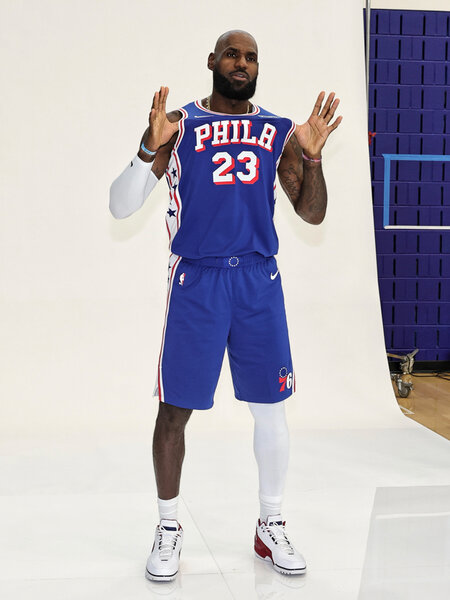 LeBron James wearing his Philadelphia 76ers jersey standing on a white step and repeat.