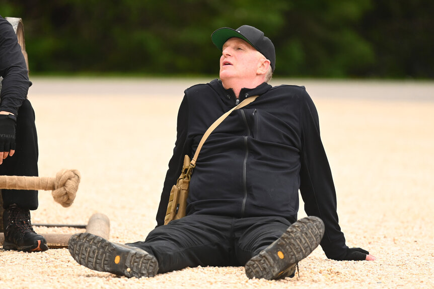 Michael Rapaport wearing all black while sitting on the ground during The Traitors