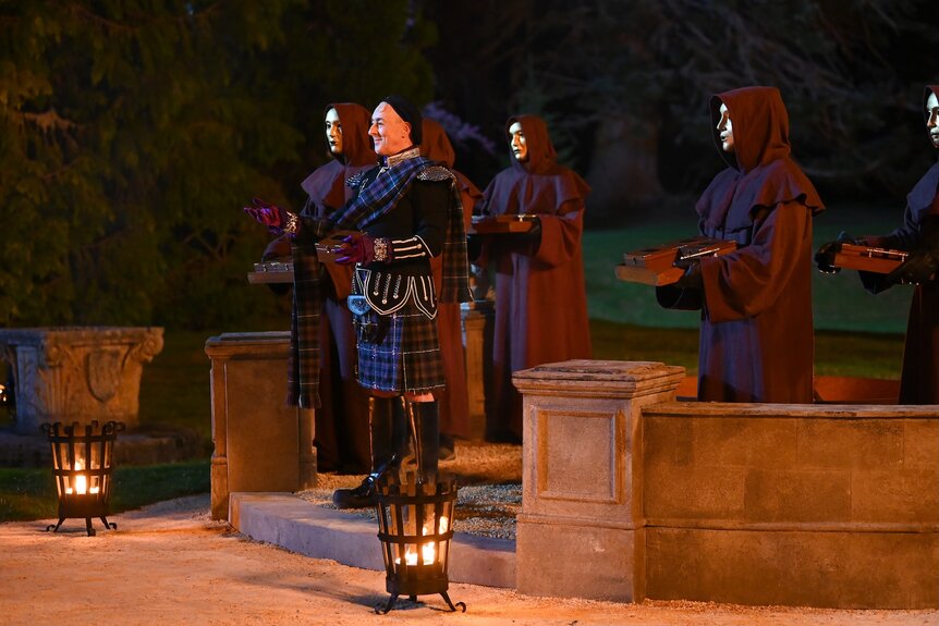 Alan Cumming stands next to masked and cloaked strangers on The Traitors Episode 401.