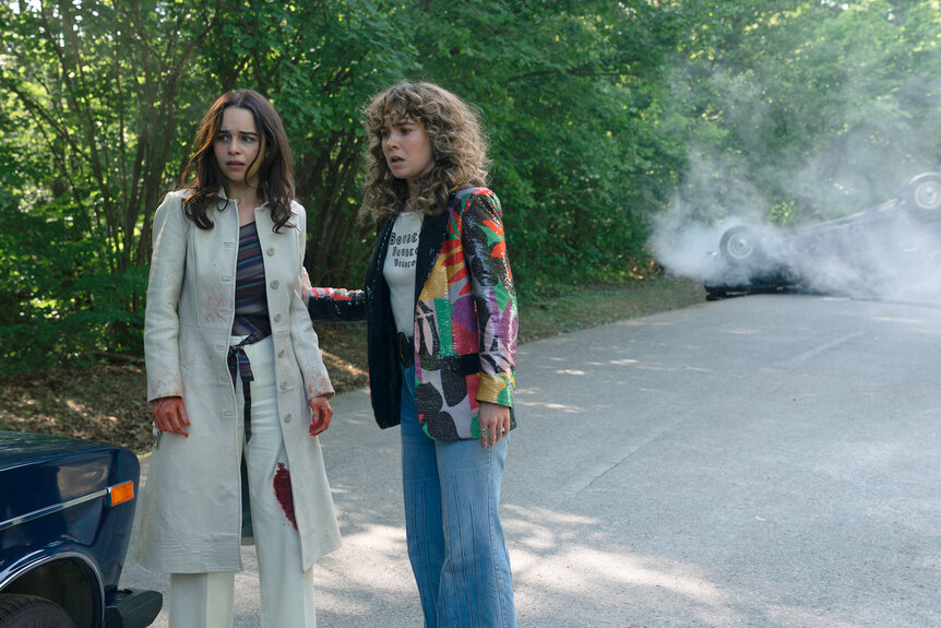 Bea and Twila standing outside by a car and smoke behind them in PONIES Season 1 Episode 8.