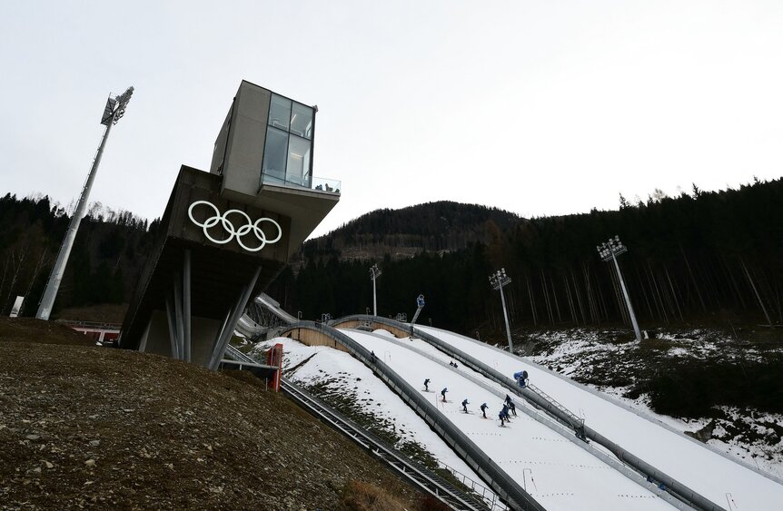Staff members prepare the ski jumping slope for the Milano Cortina 2026 Winter Olympics.
