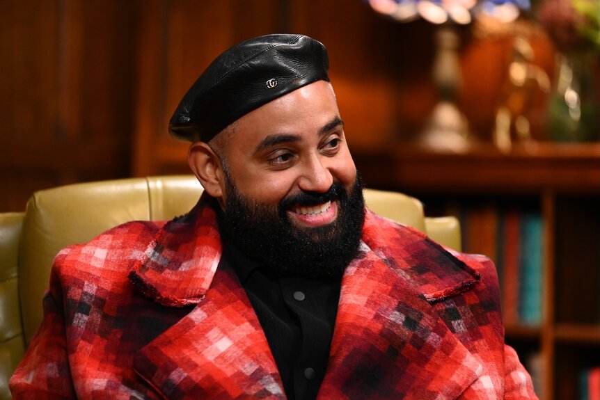 Yamil “Yam Yam” Arocho smiles in a red patterned coat on The Traitors Episode 401.