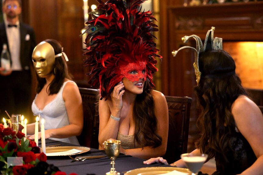 Three women wearing elaborate masks sitting an ornate dinner table on RHORI