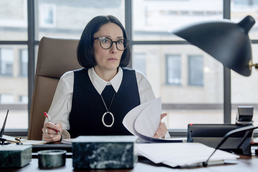 Terry (Sian Clifford) sitting at a desk in The Miniature Wife Season 1.