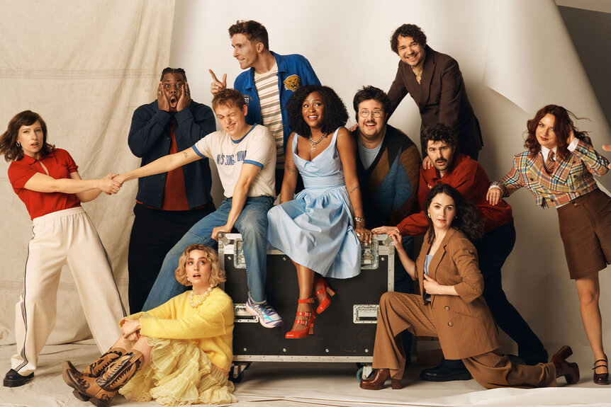 The SNL cast posing in front of a cream backdrop.