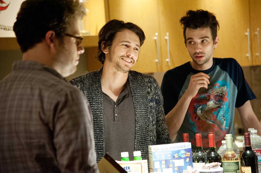 Seth Rogen, James Franco, and Jay Baruchel talking around a table of drinks in This Is The End (2013).