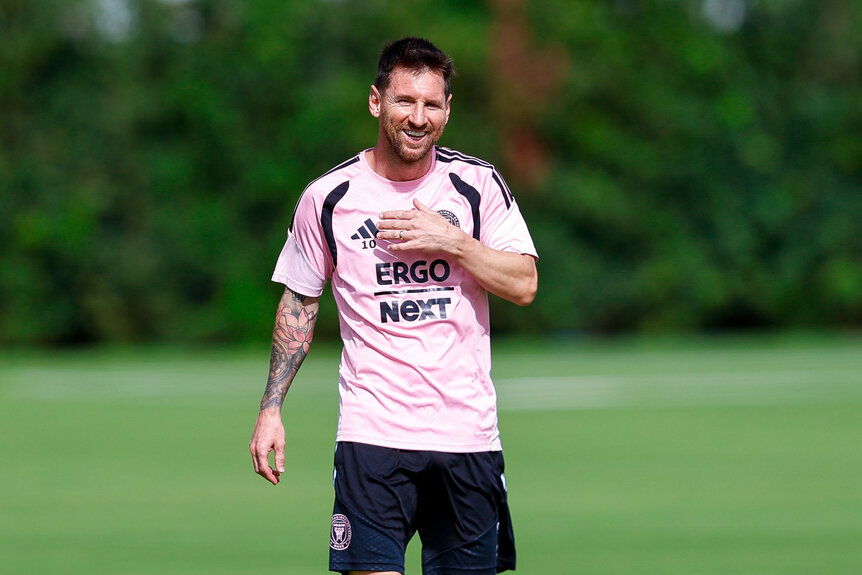 Lionel Messi wearing a pink jersey and standing in a grassy field.