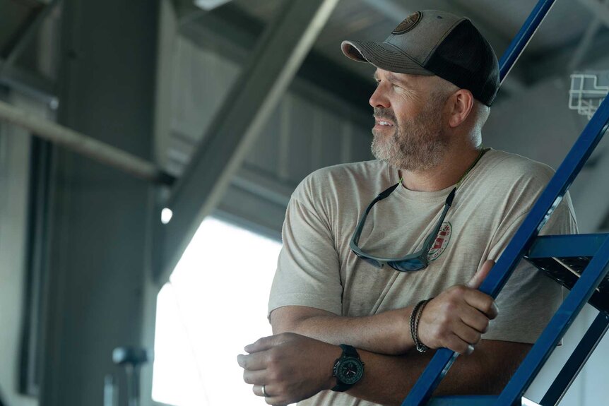 Dan with his arms crossed leaning on a ladder in M.I.A. Season 1.
