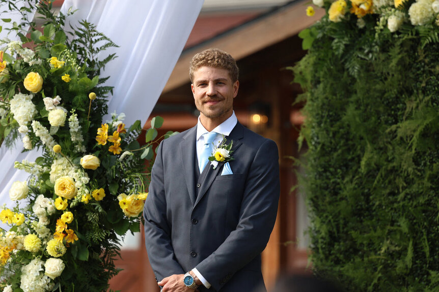 Adam Dehmlow wearing a suit standing in front of a floral arrangement during Married at First Sight