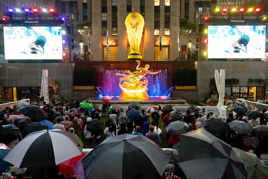 Soccer fans holding umbrellas in the rain to watch the United States play Belgium in the World Cup's Round of 16 at Rockefeller Center.