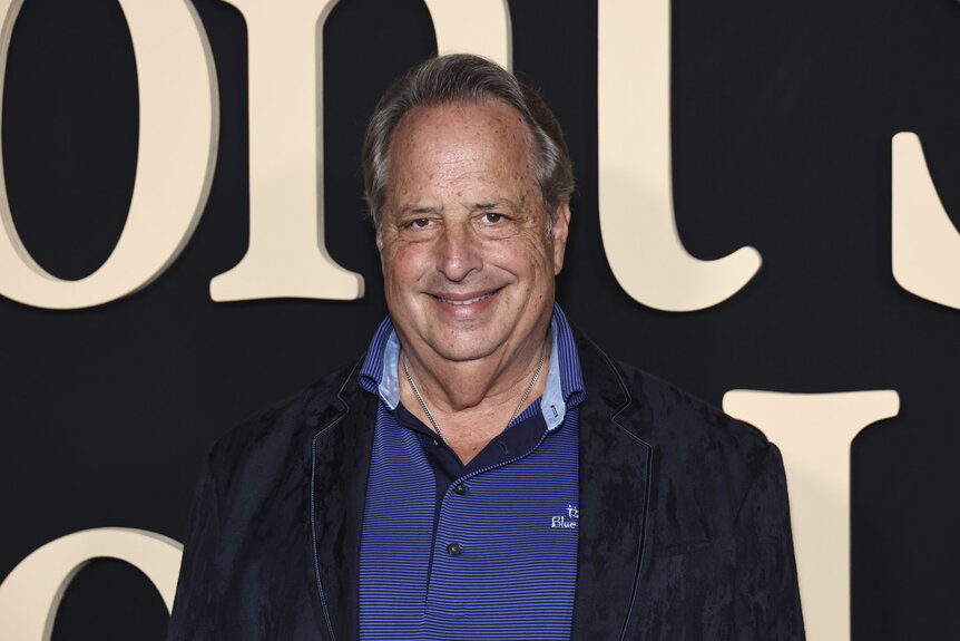 Jon Lovitz posing in front of a step and repeat.