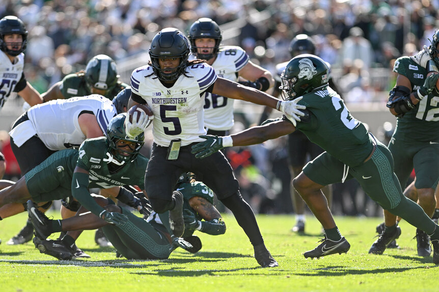 Northwestern Wildcats running back Joseph Himon II carries the ball and stiff-arms Michigan State Spartans safety Devin Vaught during a football game.